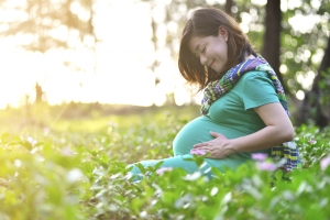 Beautiful pregnant Asian woman feeling lovely and smile in the park with warm light sunset