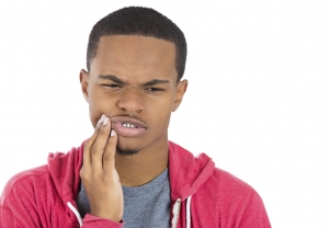 Closeup portrait of young man in red hoodie with tooth ache crown problem about to cry from pain touching outside mouth with hand, isolated white background. Negative emotion facial expression feeling
