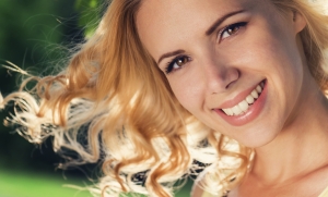 Close up of blond woman with curly hair flipping them in the air in yellow singlet in green nature. Sunny summer.