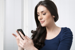 Young beautiful brunette lady touching and browsing her smart phone at home