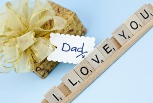 Suffolk, Virginia, USA - May 10, 2011: A horizontal studio shot of Hasbro Scrabble tiles lined up in a wooden Scrabble tile rack to spell the message I Love You. Behind the rack of letters is a gift with a bow and gift tag marked Dad.