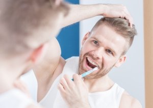 Reflection of handsome guy brushing his teeth