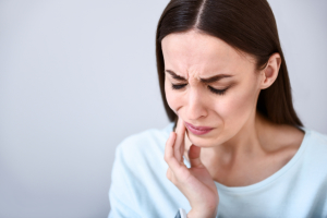 Serious problem. Cheerless sick woman touching her jaw and having a tooth ache while standing isolated on white background