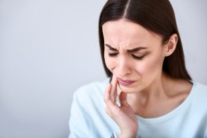 Serious problem. Cheerless sick woman touching her jaw and having a tooth ache while standing isolated on white background