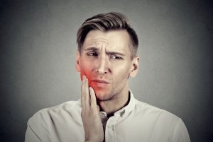 Closeup portrait young man with sensitive toothache crown problem about to cry from pain touching outside mouth with hand isolated on gray background. Negative human emotion face expression feeling