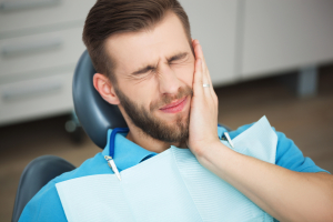 Shot of a young man with tooth pain while sitting in a dentist's chair.