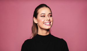 Portrait of caucasian female model standing and smiling against pink background. Beautiful woman with perfect skin and makeup looking away.